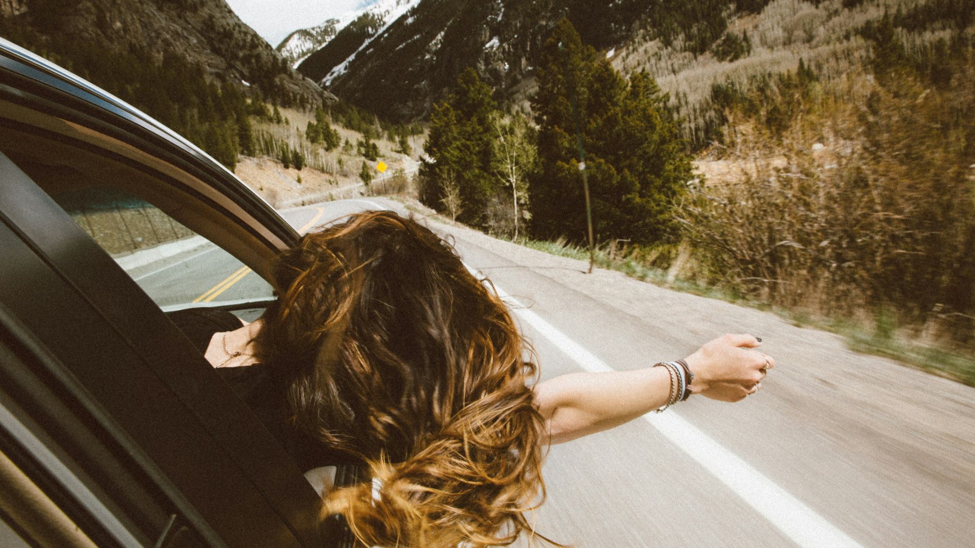 woman riding on vehicle putting her head and right arm outside the window while travelling the road