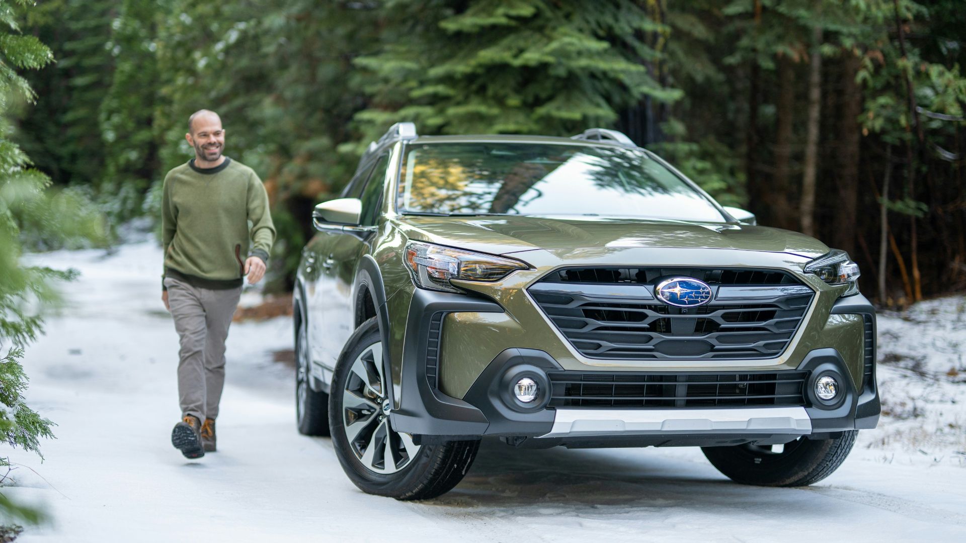 A man walking down a snow covered road next to a car