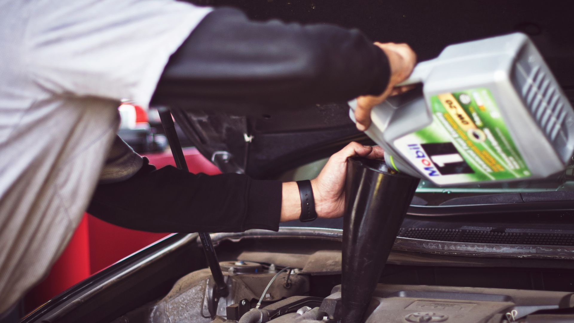 man refilling motor oil on car engine bay
