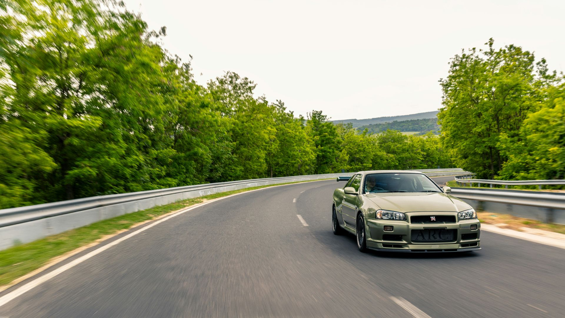 A silver sports car drives on a winding road.