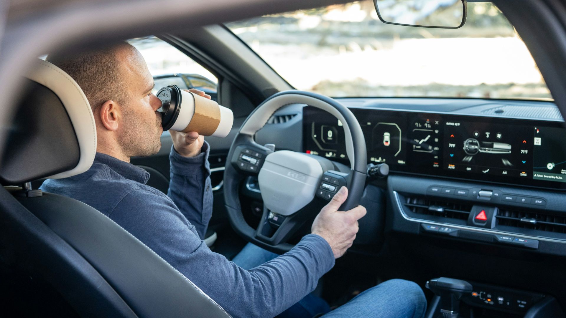 A man driving a car with a cup in his hand