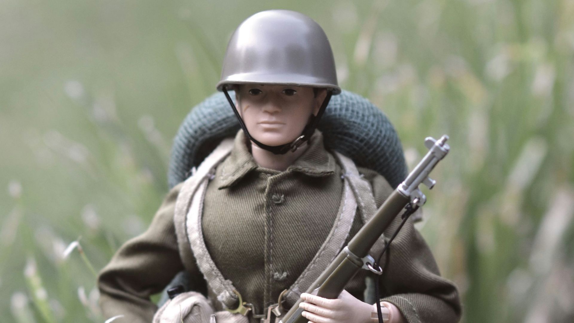 A toy soldier in a field with a rifle