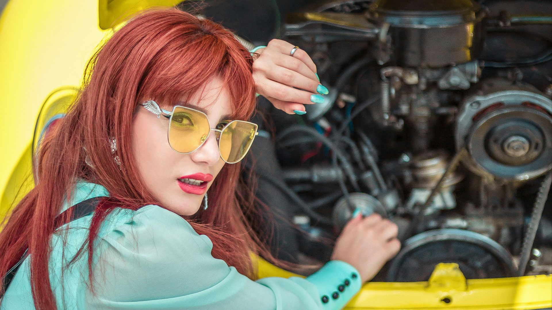 a woman with red hair and sunglasses sitting on the ground next to a yellow car