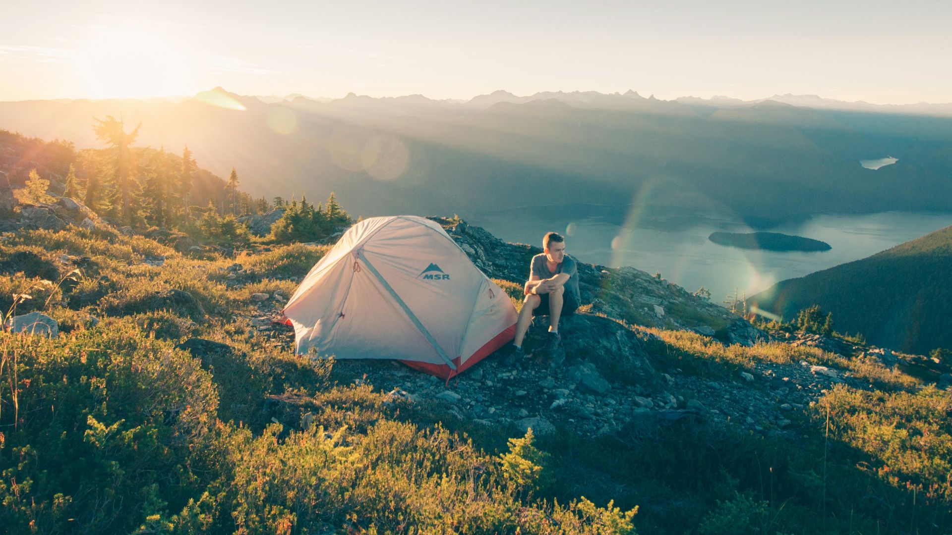 man sitting on stone beside white camping tent