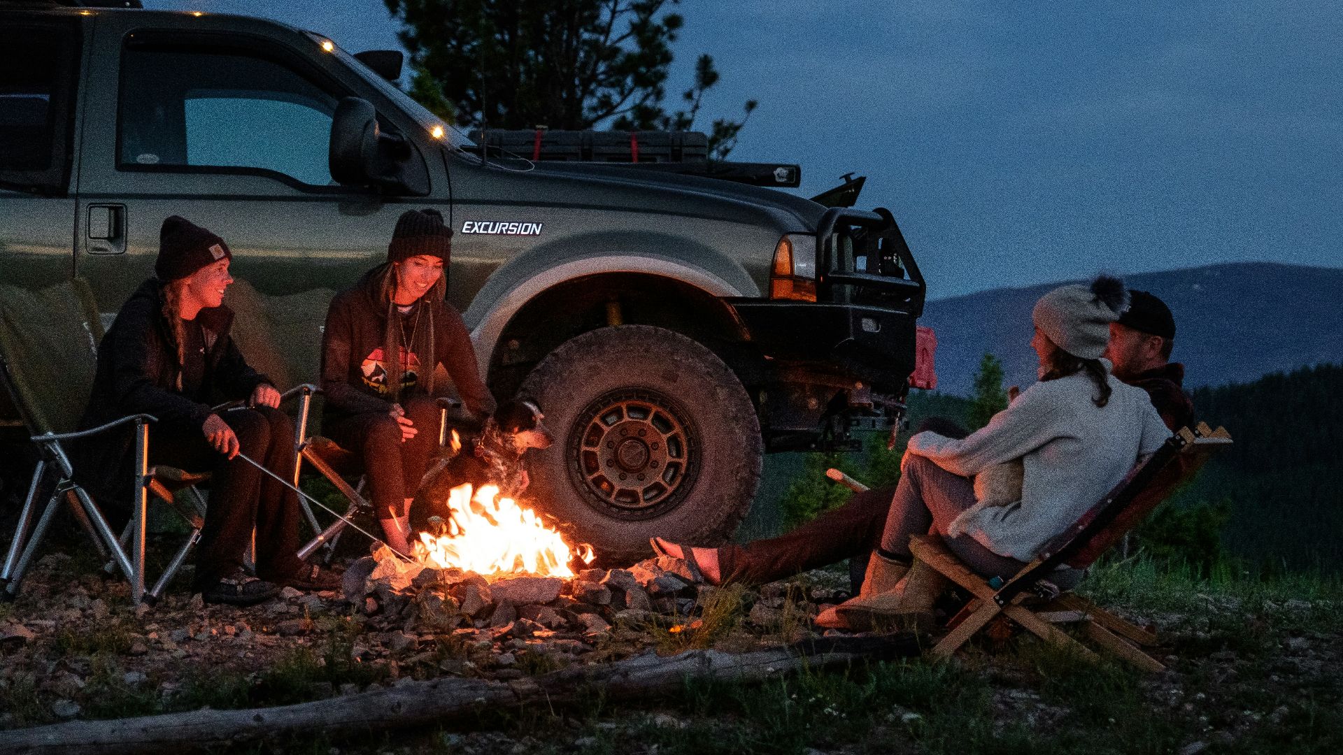 man in white shirt sitting on brown wooden chair near black suv during night time