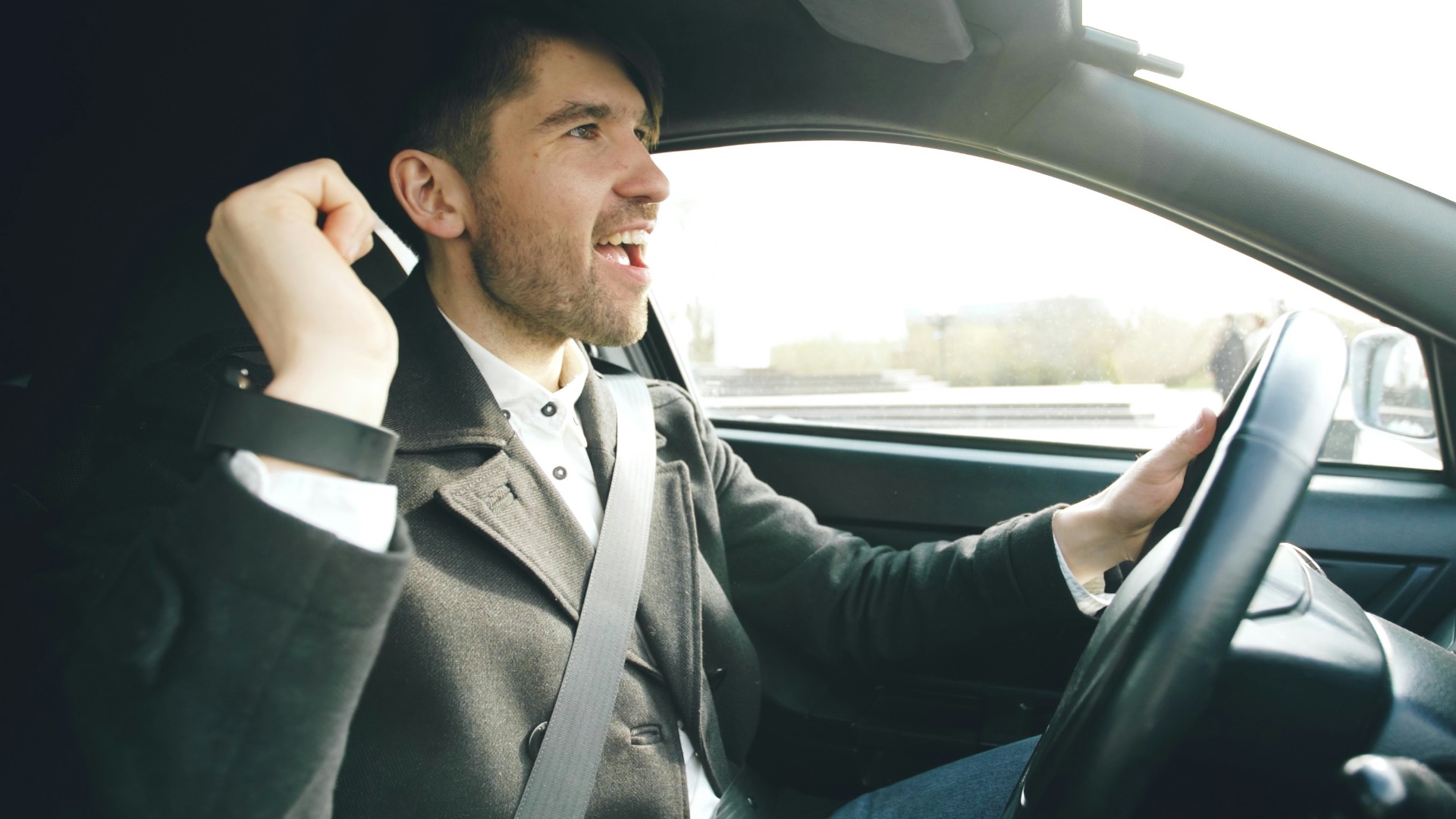 Man singing and driving a car enthusiastically.