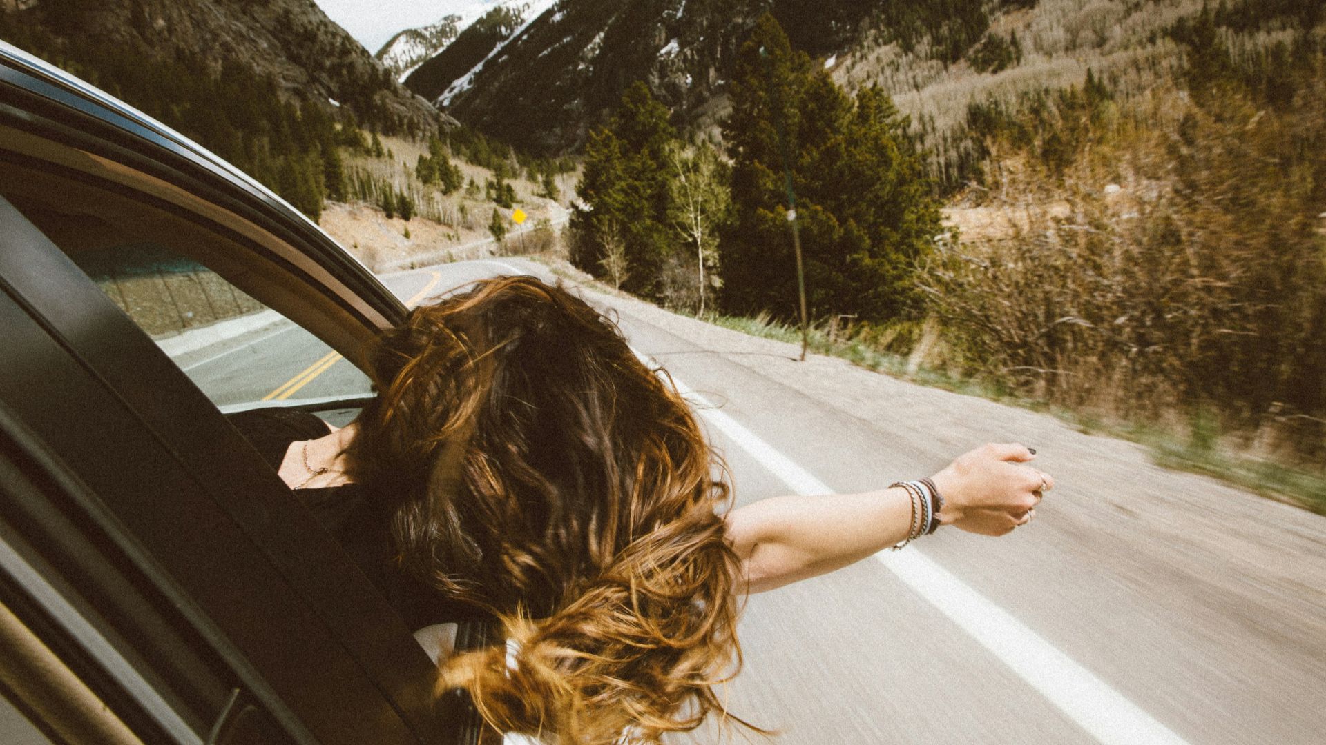 woman riding on vehicle putting her head and right arm outside the window while travelling the road