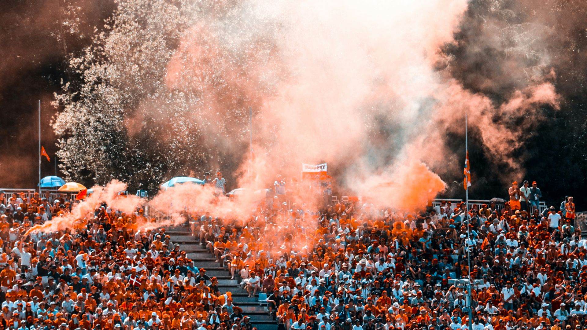 aerial photo of people sitting on stadium with orange smokes above them