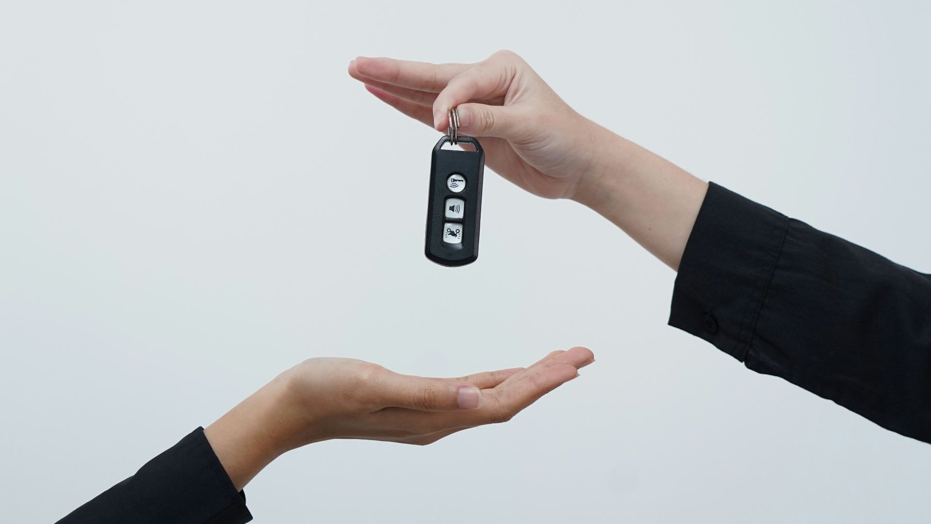 Hands exchanging a car key against a light background