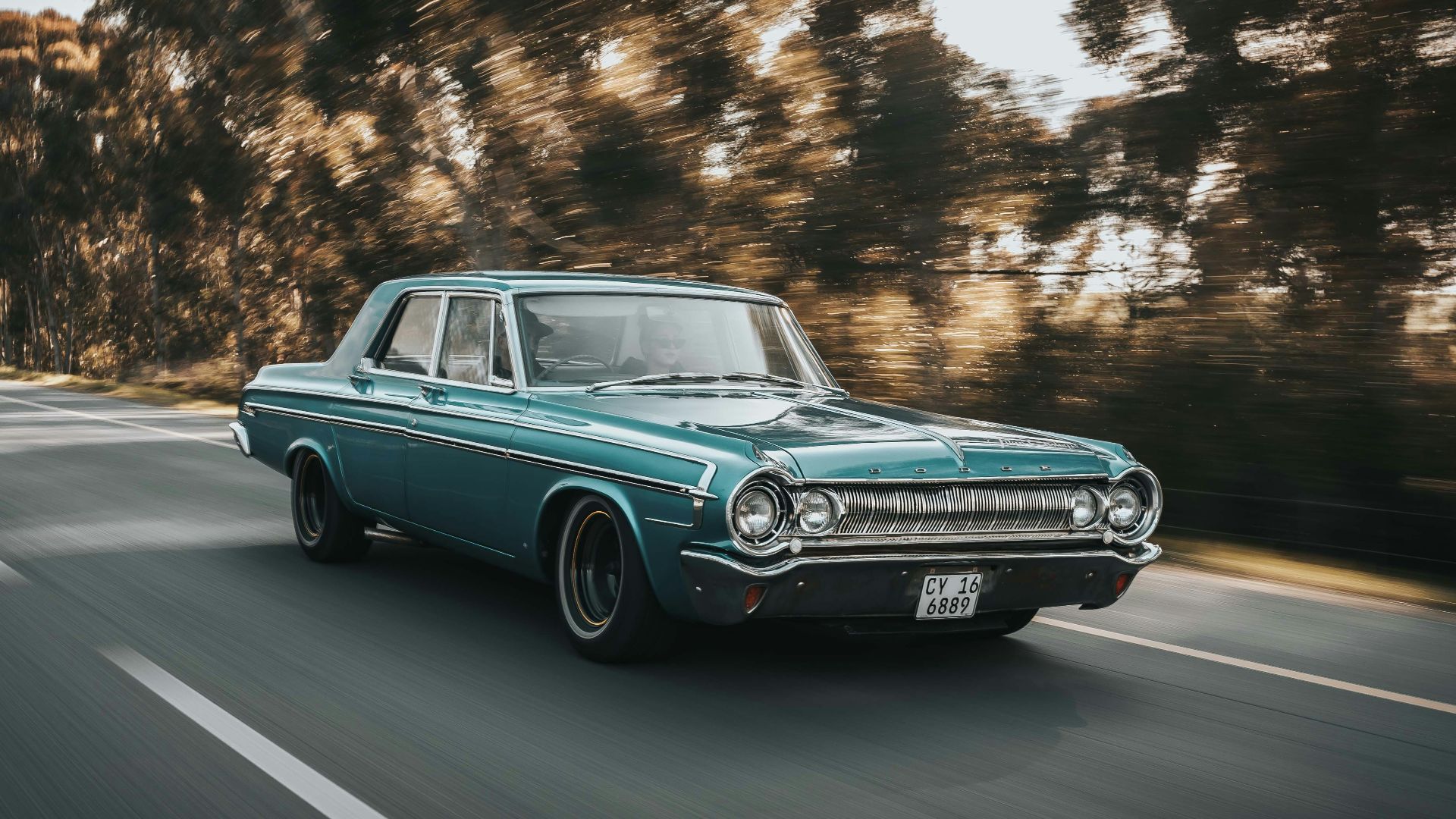teal sedan on roadway beside the trees