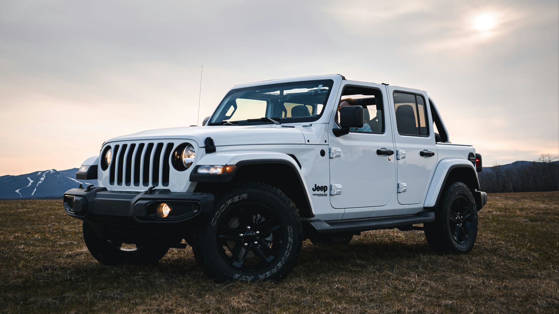 white jeep wrangler on green grass field under white clouds during daytime