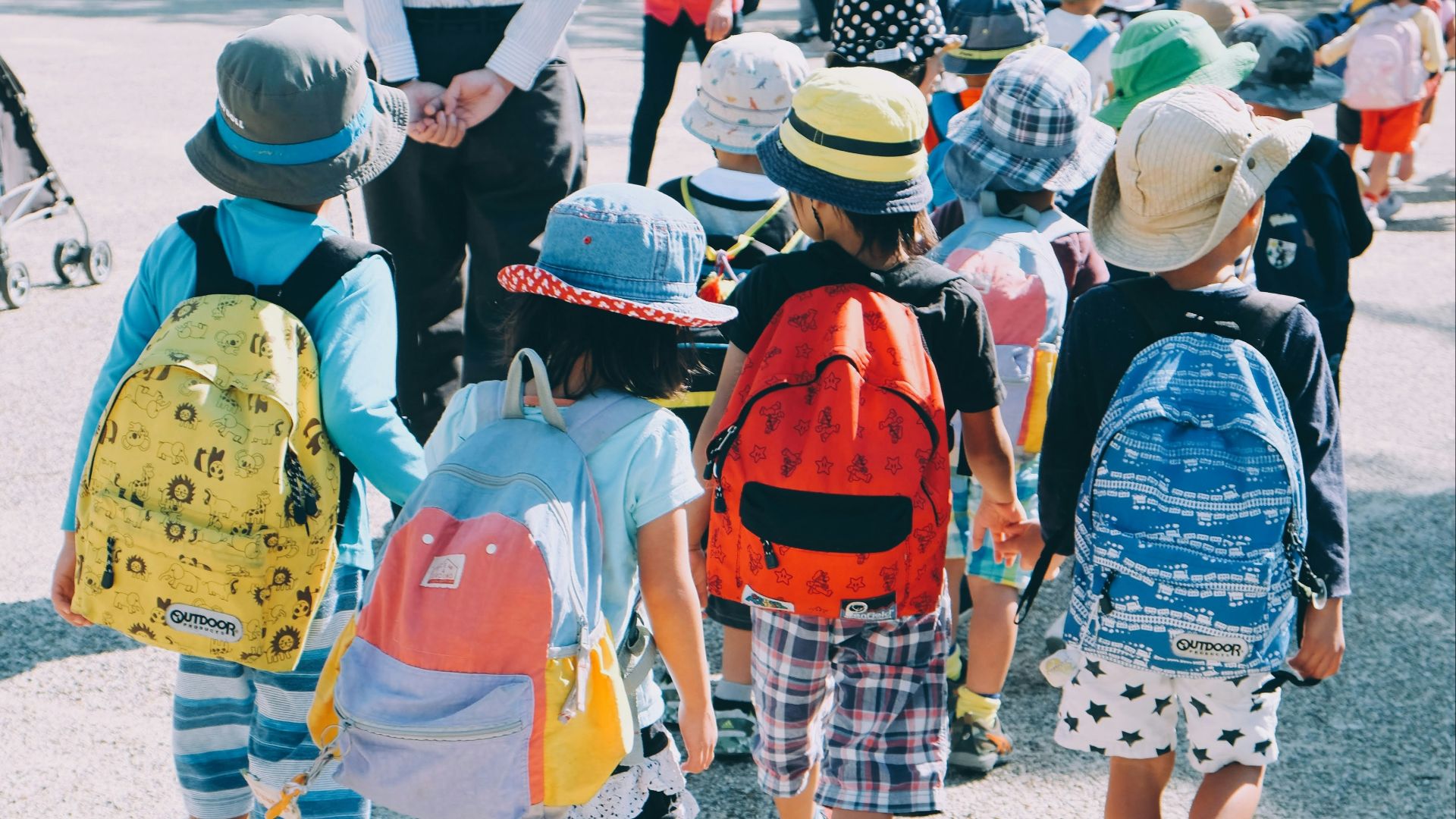 group of people wearing white and orange backpacks walking on gray concrete pavement during daytime