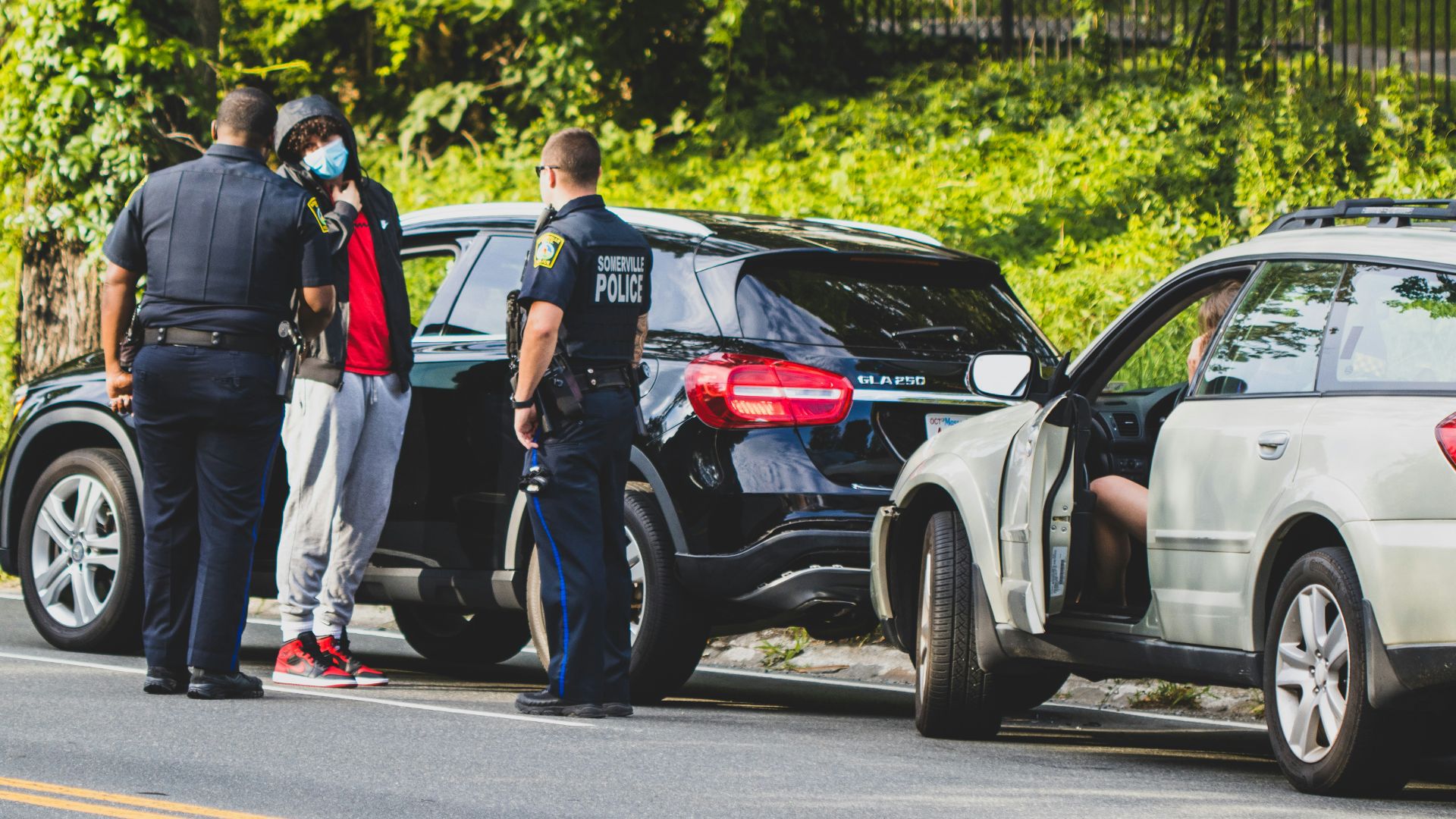 man in black t-shirt and black pants standing beside black suv during daytime