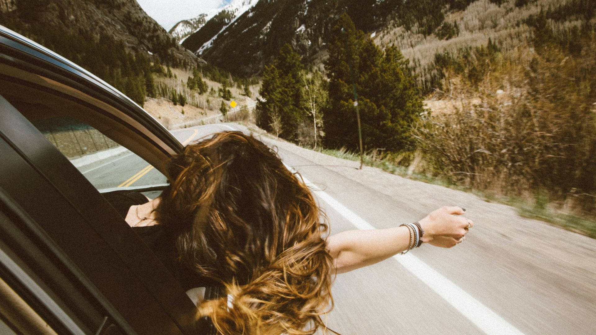 woman riding on vehicle putting her head and right arm outside the window while travelling the road