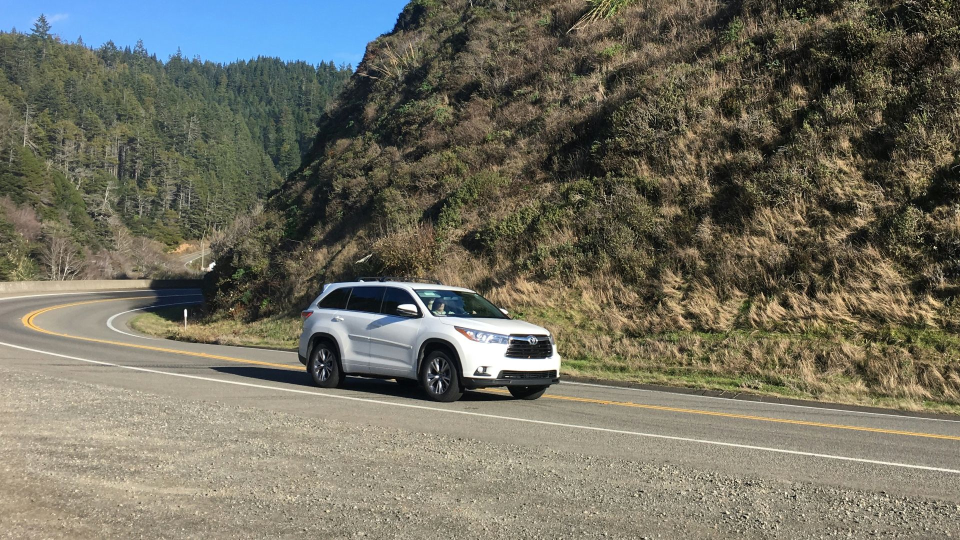 a white car driving down a curvy road next to a mountain
