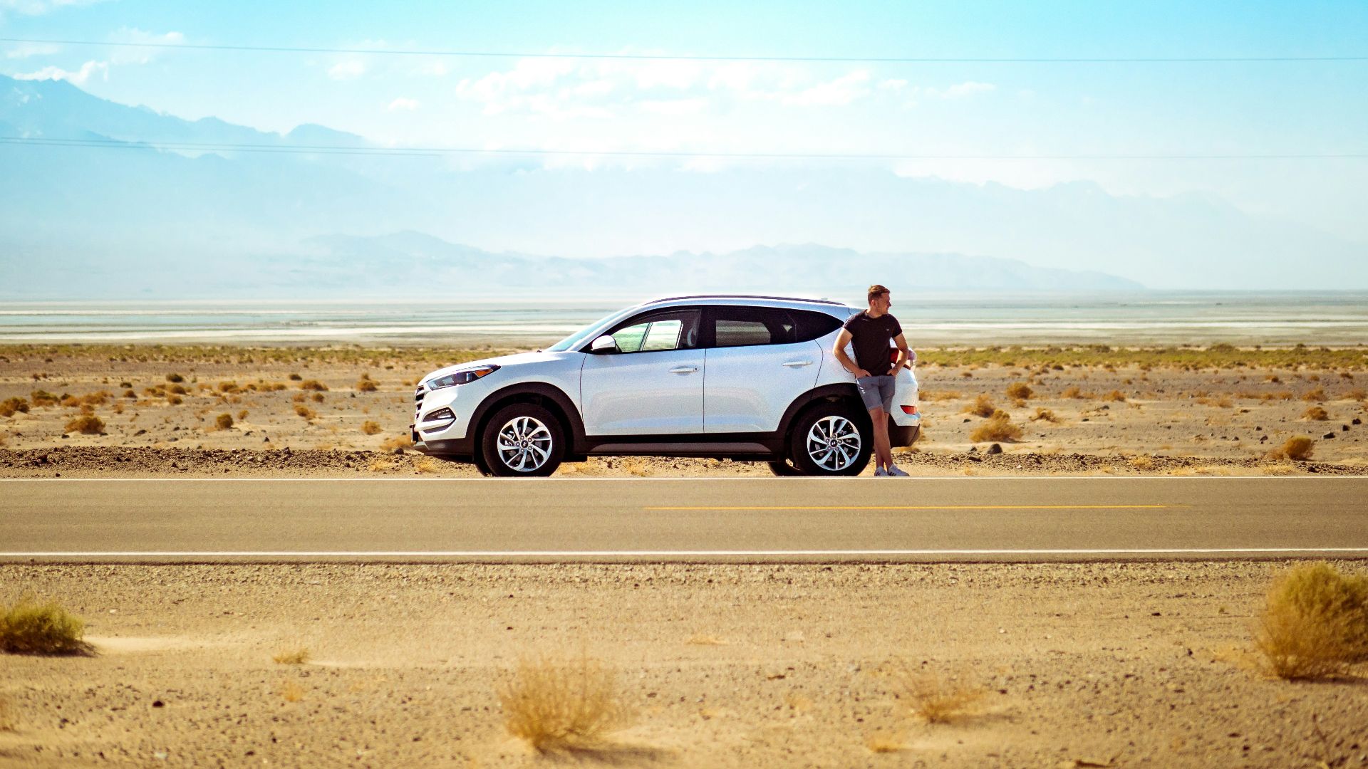man standing beside white SUV near concrete road under blue sky at daytime