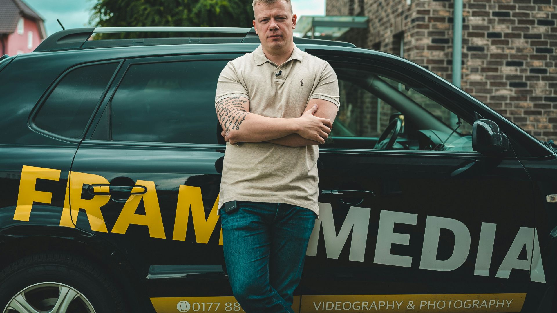 man in gray long sleeve shirt and blue denim jeans standing beside blue and yellow car