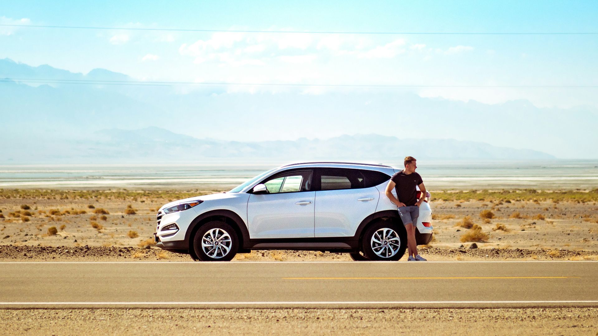 man standing beside white SUV near concrete road under blue sky at daytime