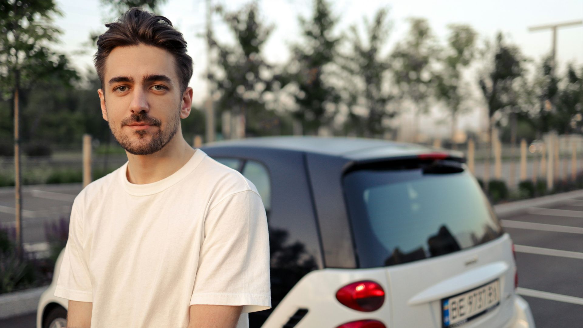 man in white crew neck t-shirt standing beside white car during daytime