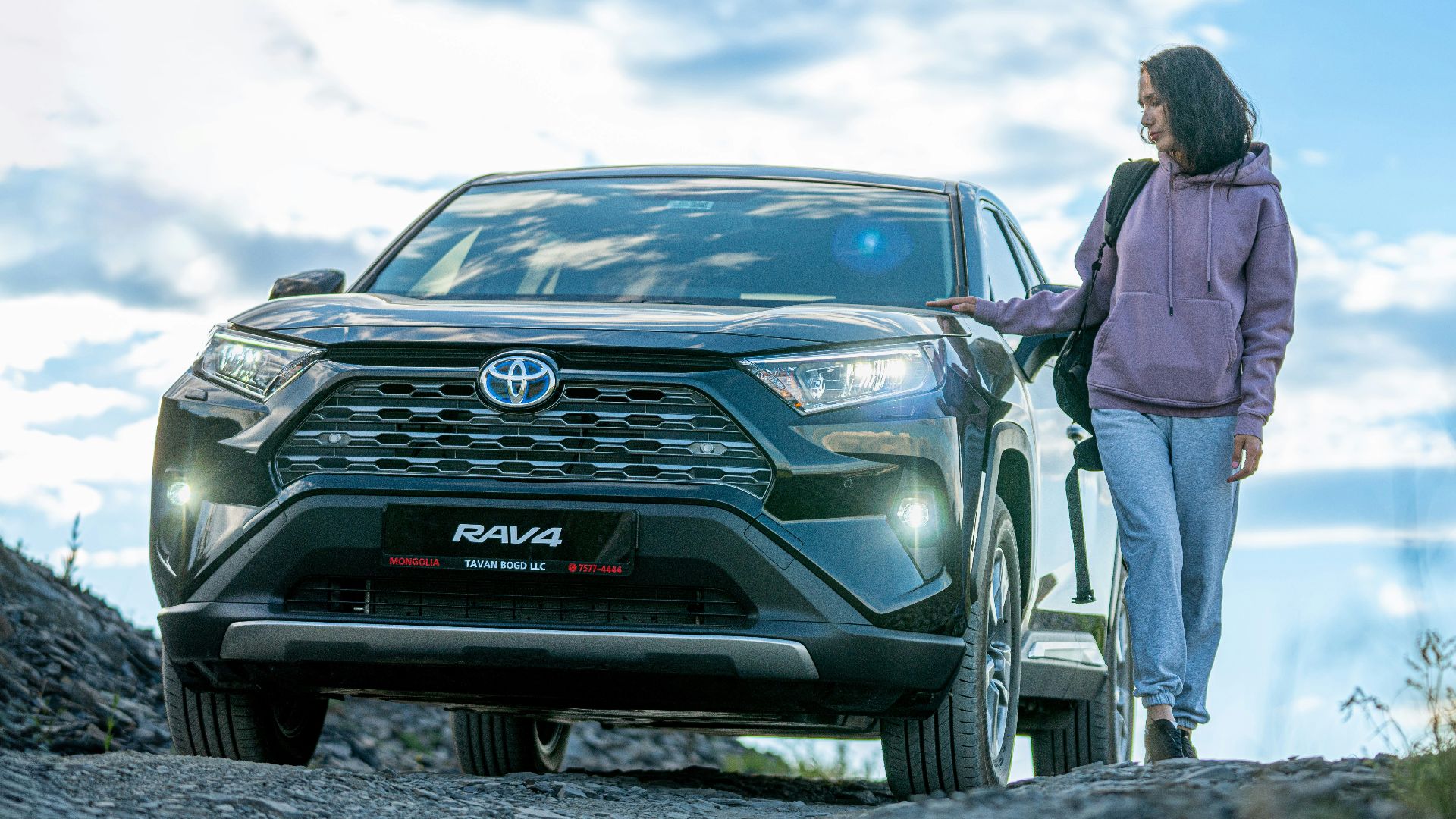 A woman standing next to a car on a dirt road