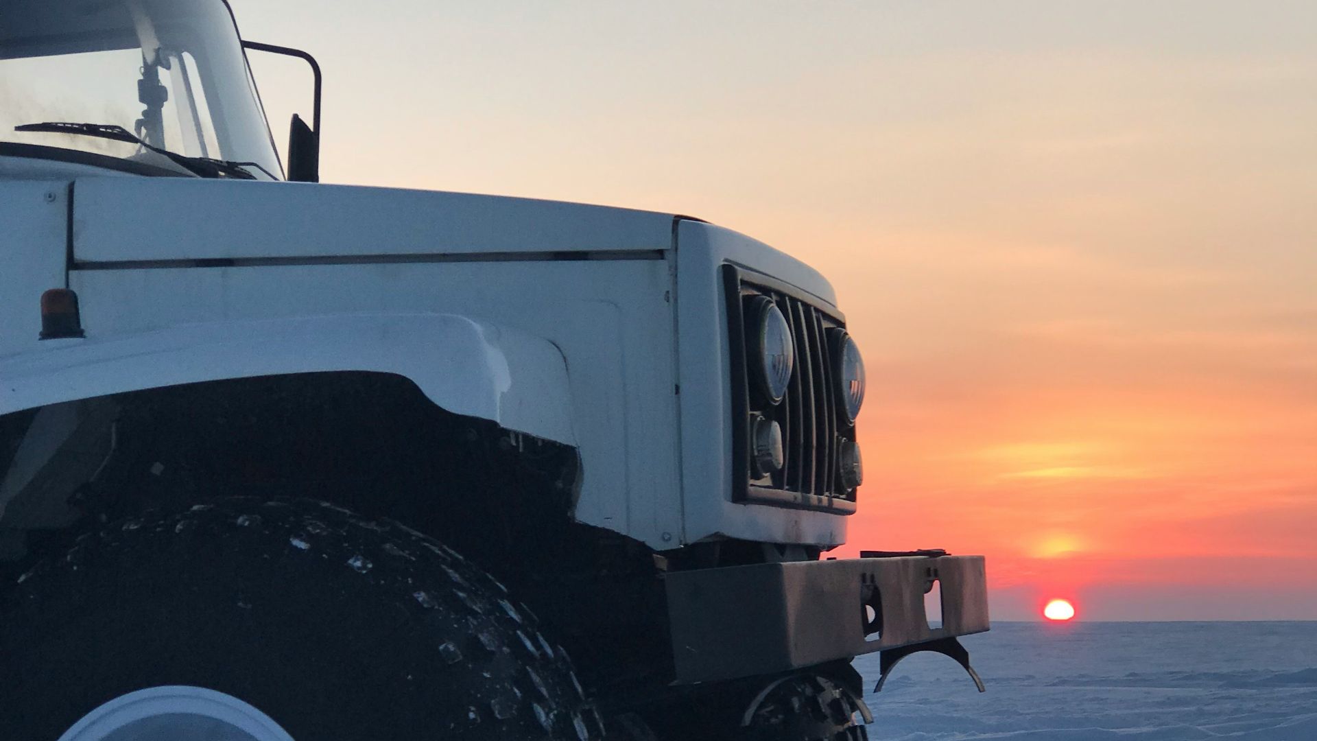 white vehicle parked on seashore with background of sunset