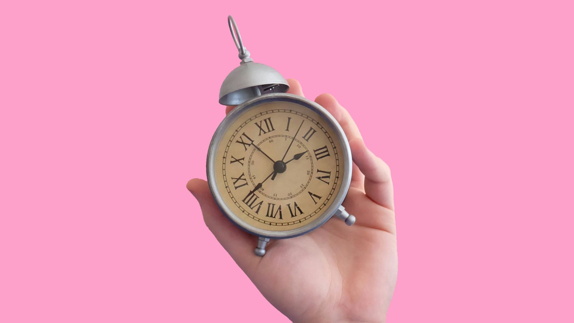 person holding gray and beige roman numeral alarm clock