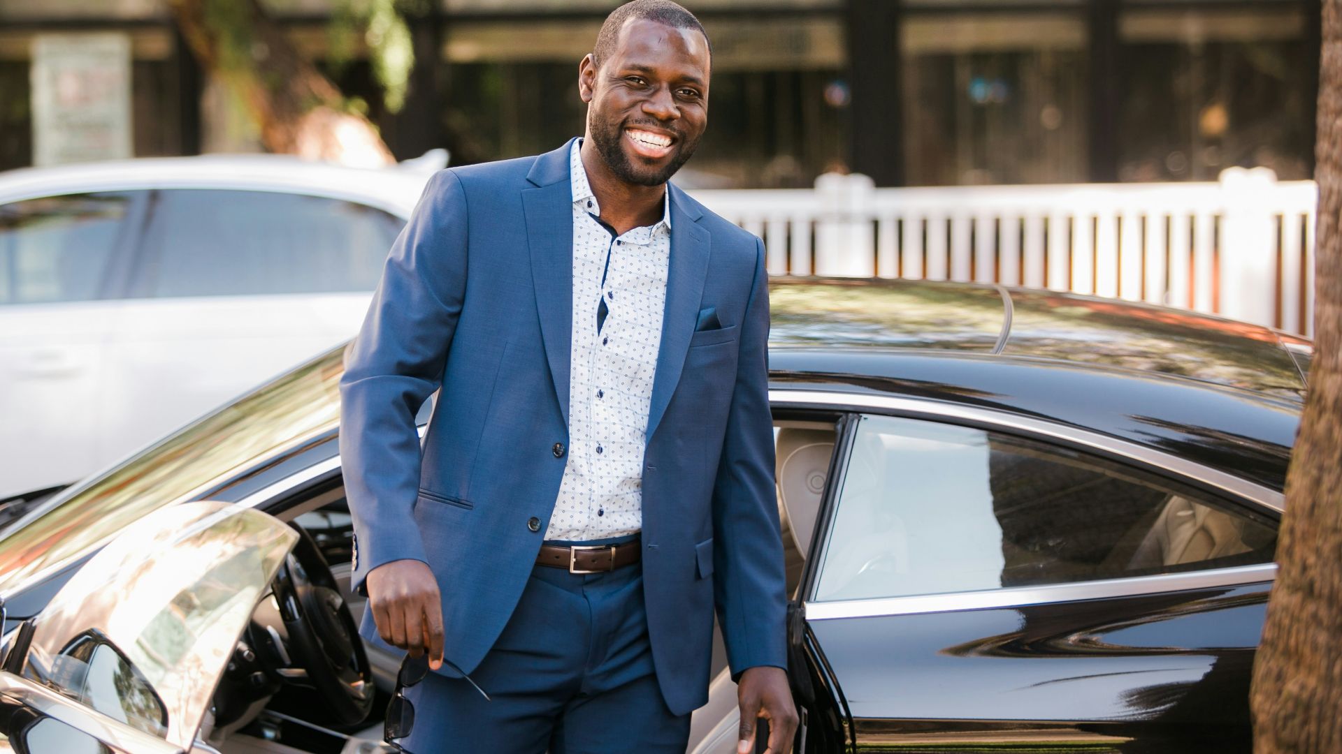 man in blue suit standing beside black car