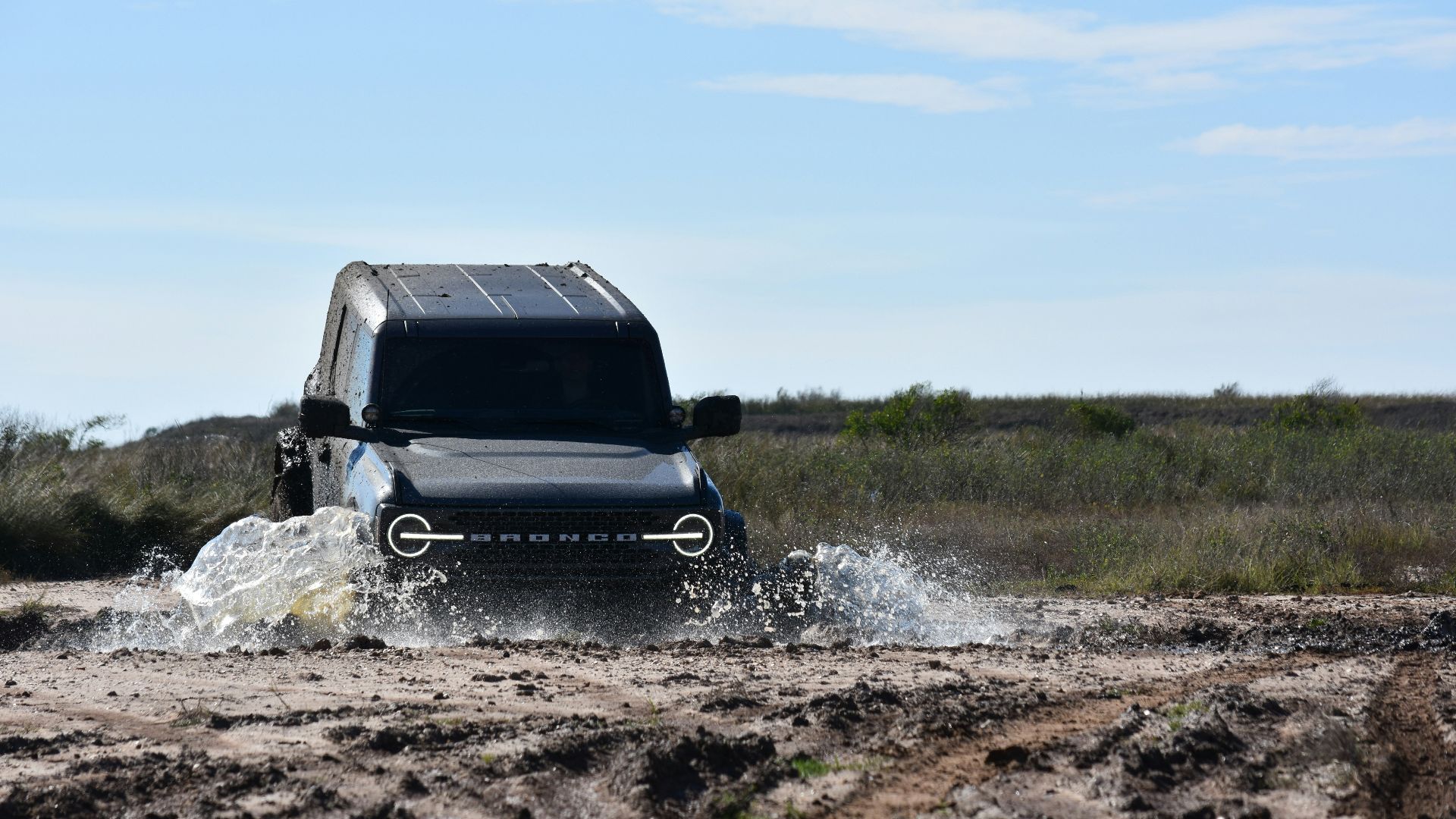 a black truck driving through a muddy field