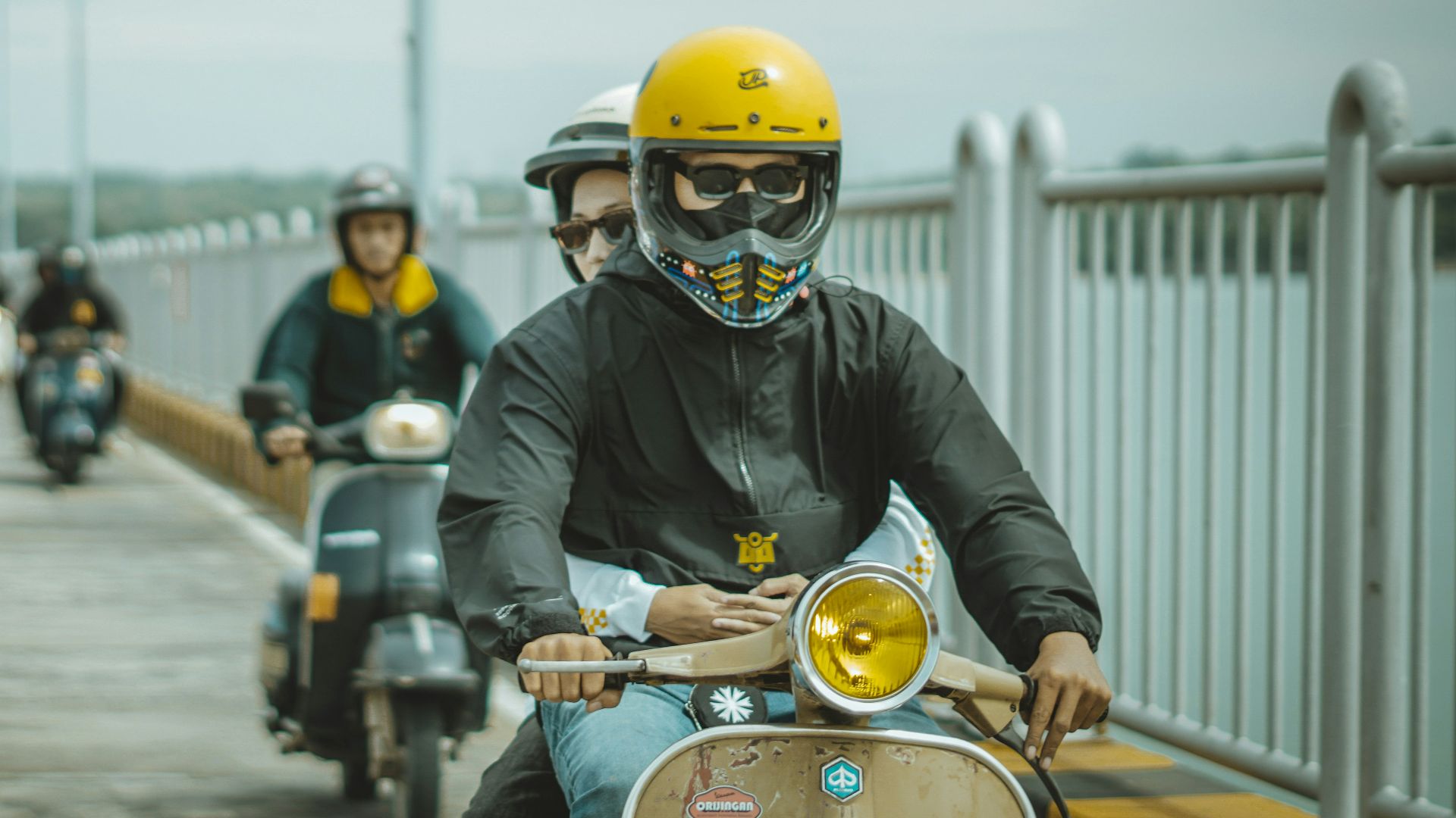 Scooter riders cruise across a bridge.