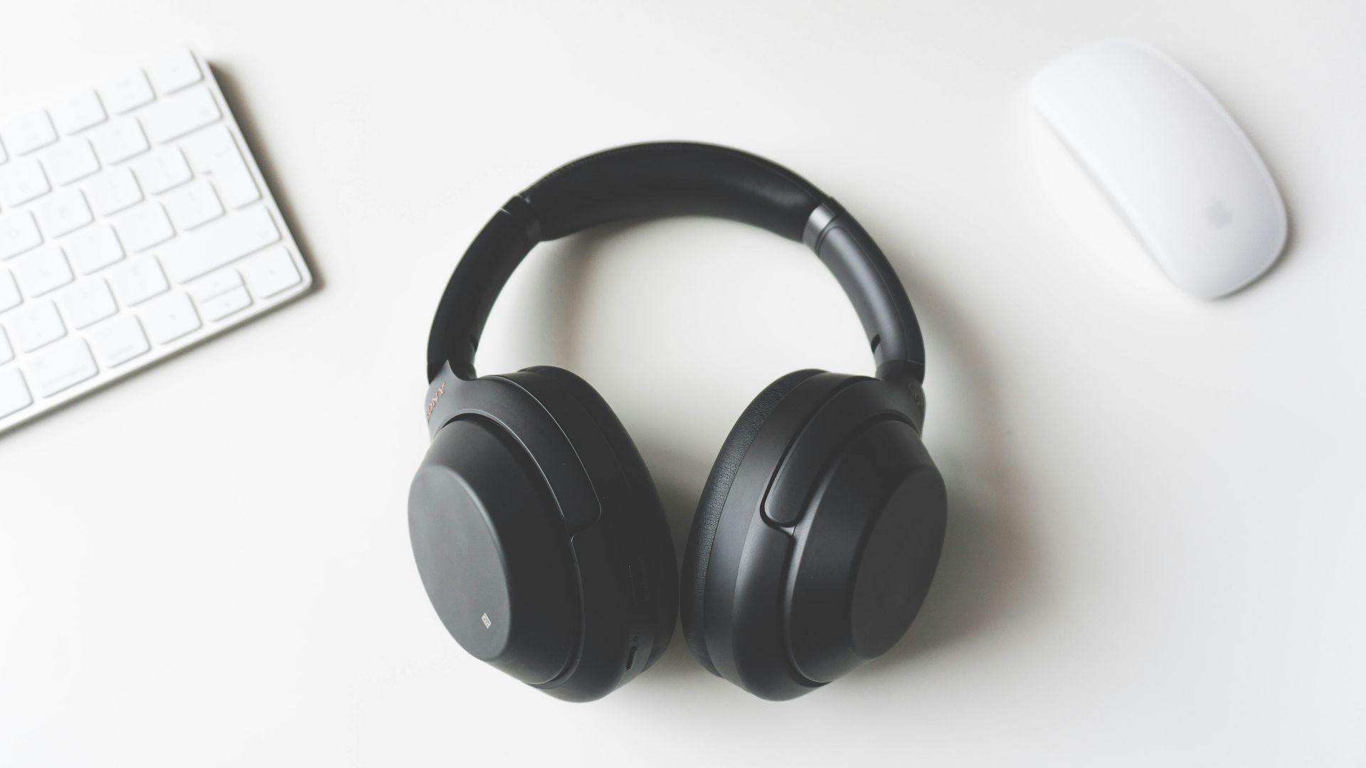 black wireless headphones between Apple Keyboard and Apple Magic Mouse on white surface