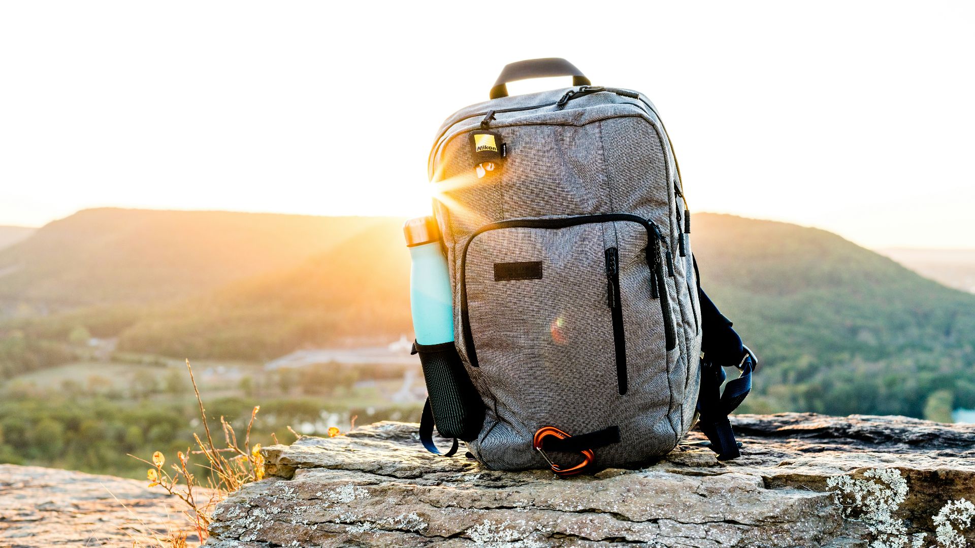 grey and black hiking backpack and cyan tumbler on grey rock during sunset