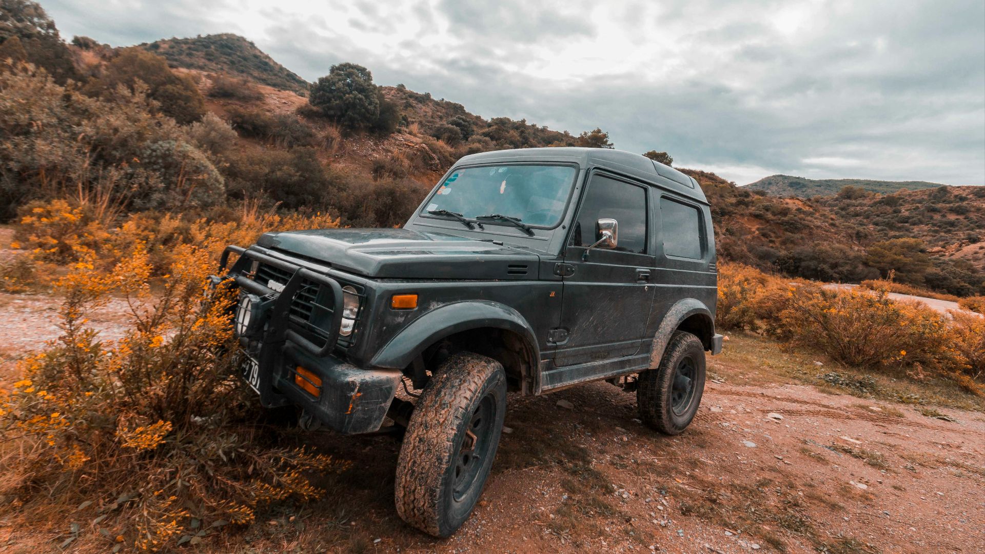 parked black SUV on dirt and plant field