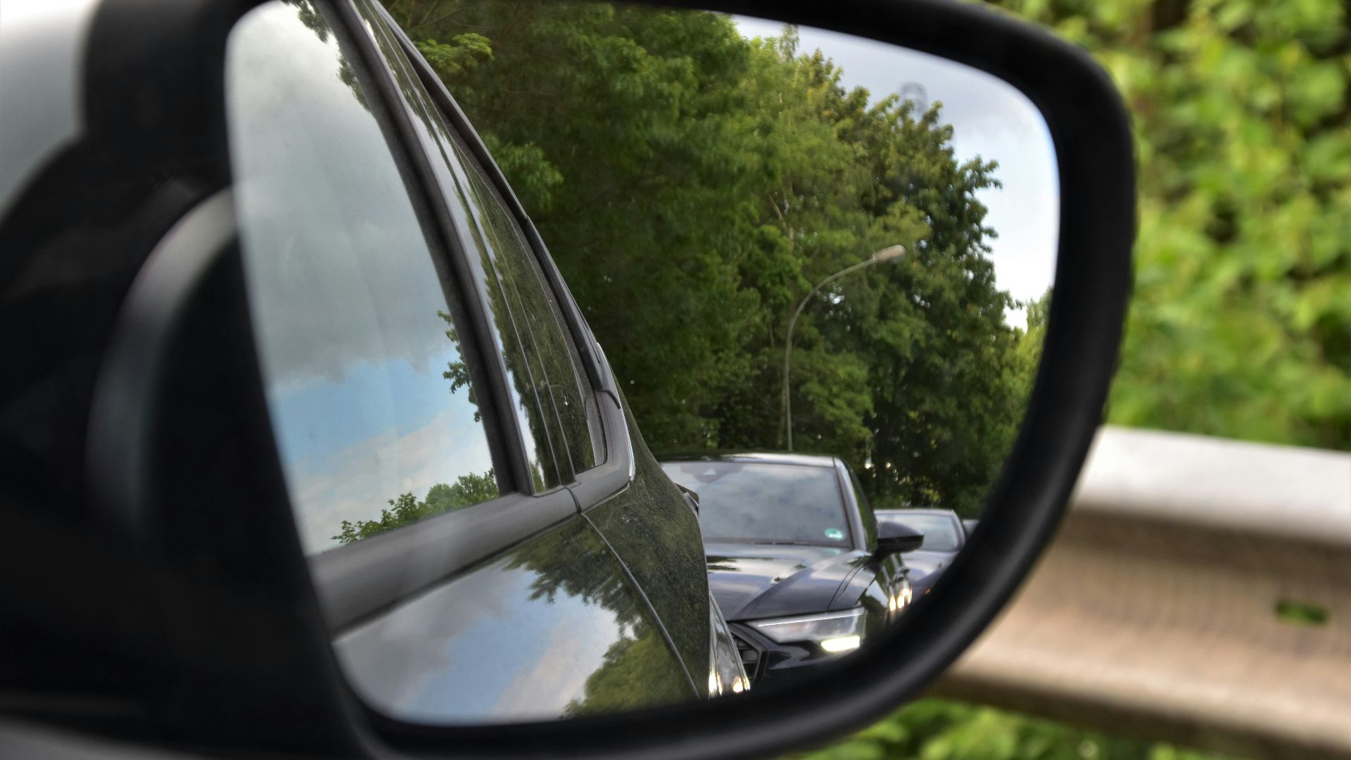 black car side mirror reflecting green trees during daytime