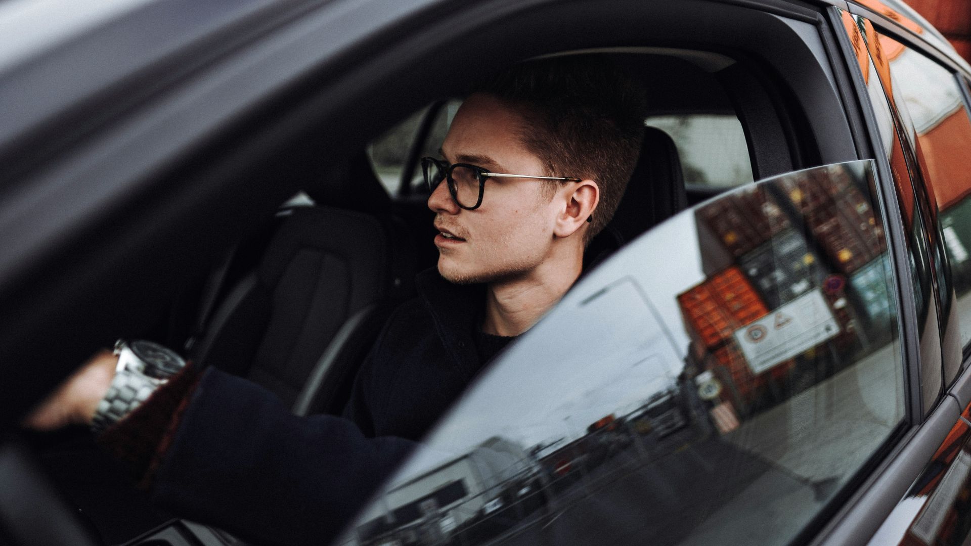 man in black jacket wearing eyeglasses sitting inside car