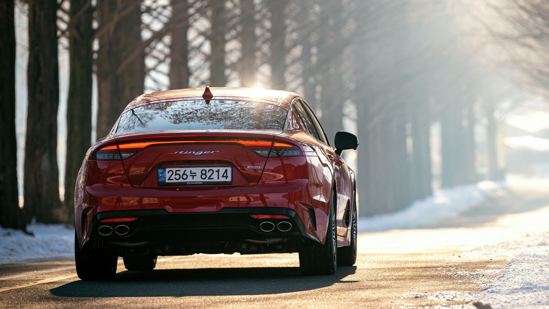 a red car driving on a road with snow on the side