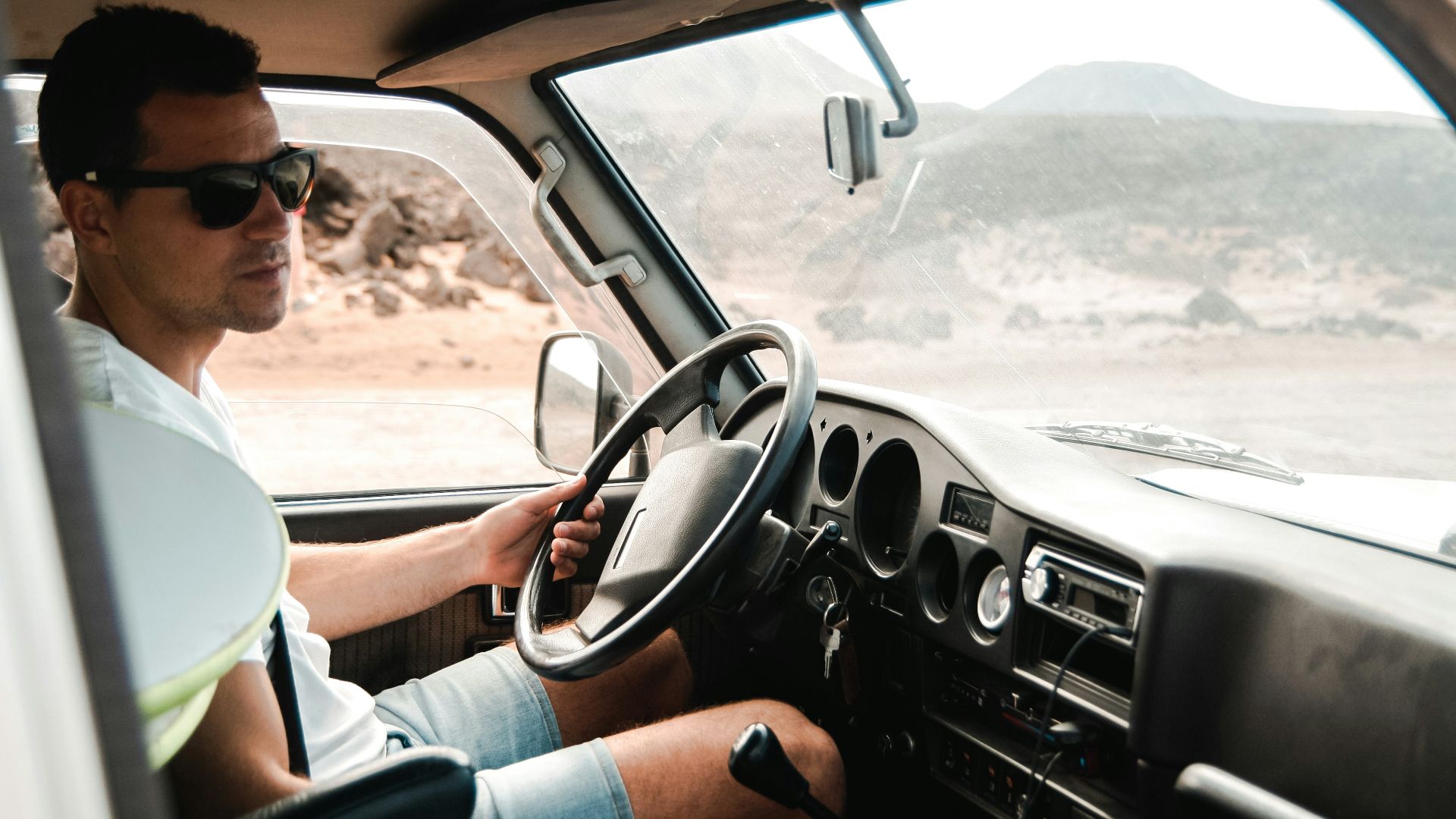 man wearing white crew-neck shirt holding steering wheel