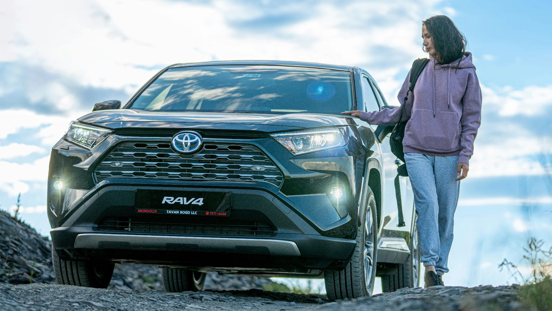 A woman standing next to a car on a dirt road