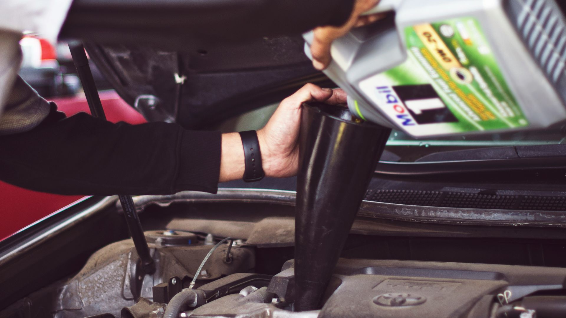 man refilling motor oil on car engine bay
