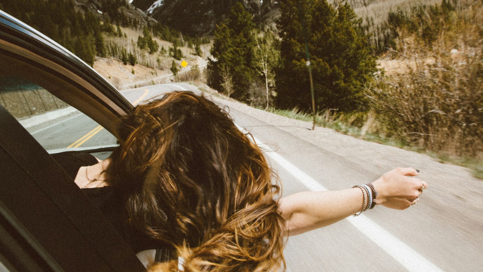 woman riding on vehicle putting her head and right arm outside the window while travelling the road