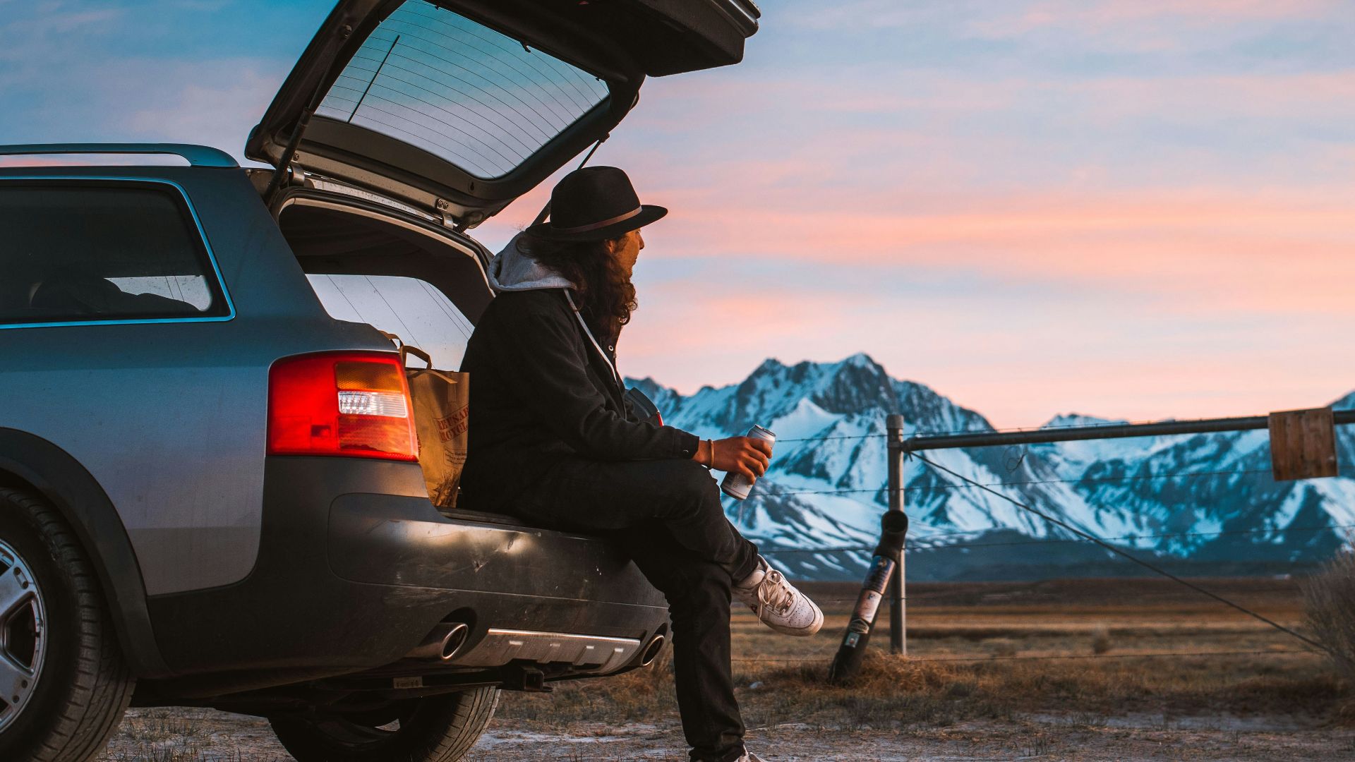man sitting on car's tail looking at ranch