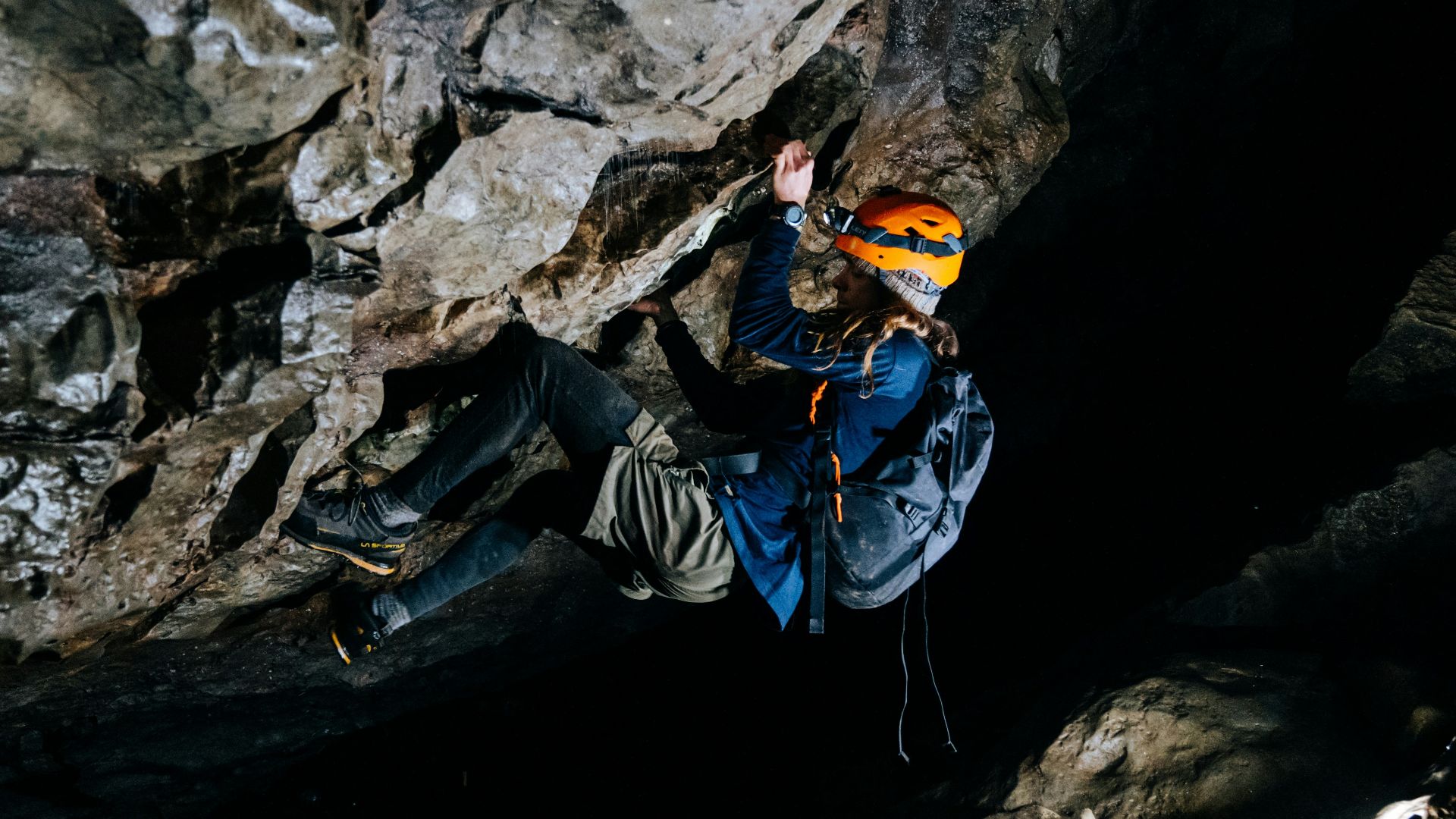 man in blue jacket and black pants sitting on rock