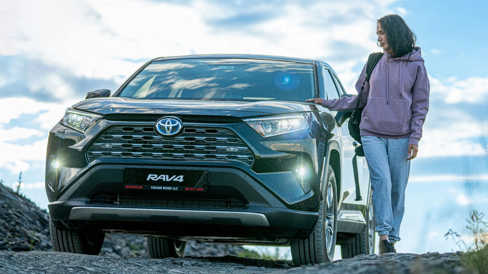A woman standing next to a car on a dirt road