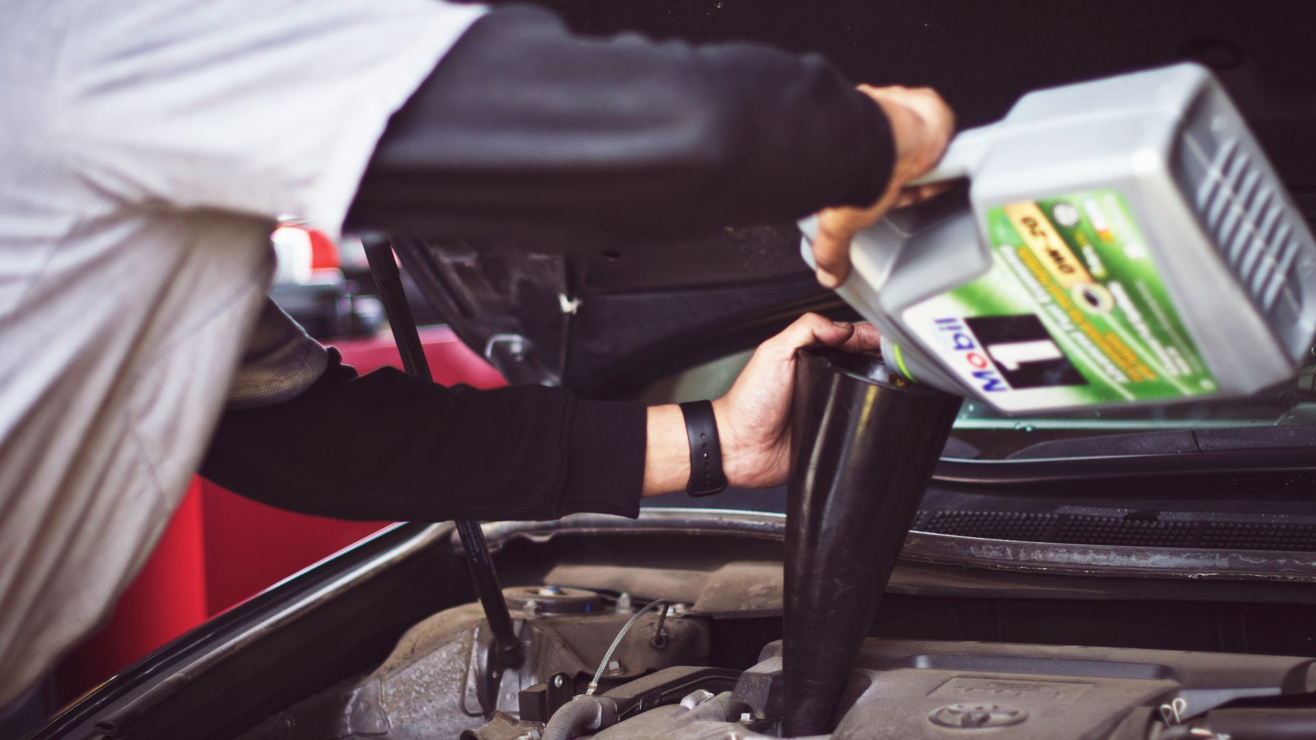 man refilling motor oil on car engine bay