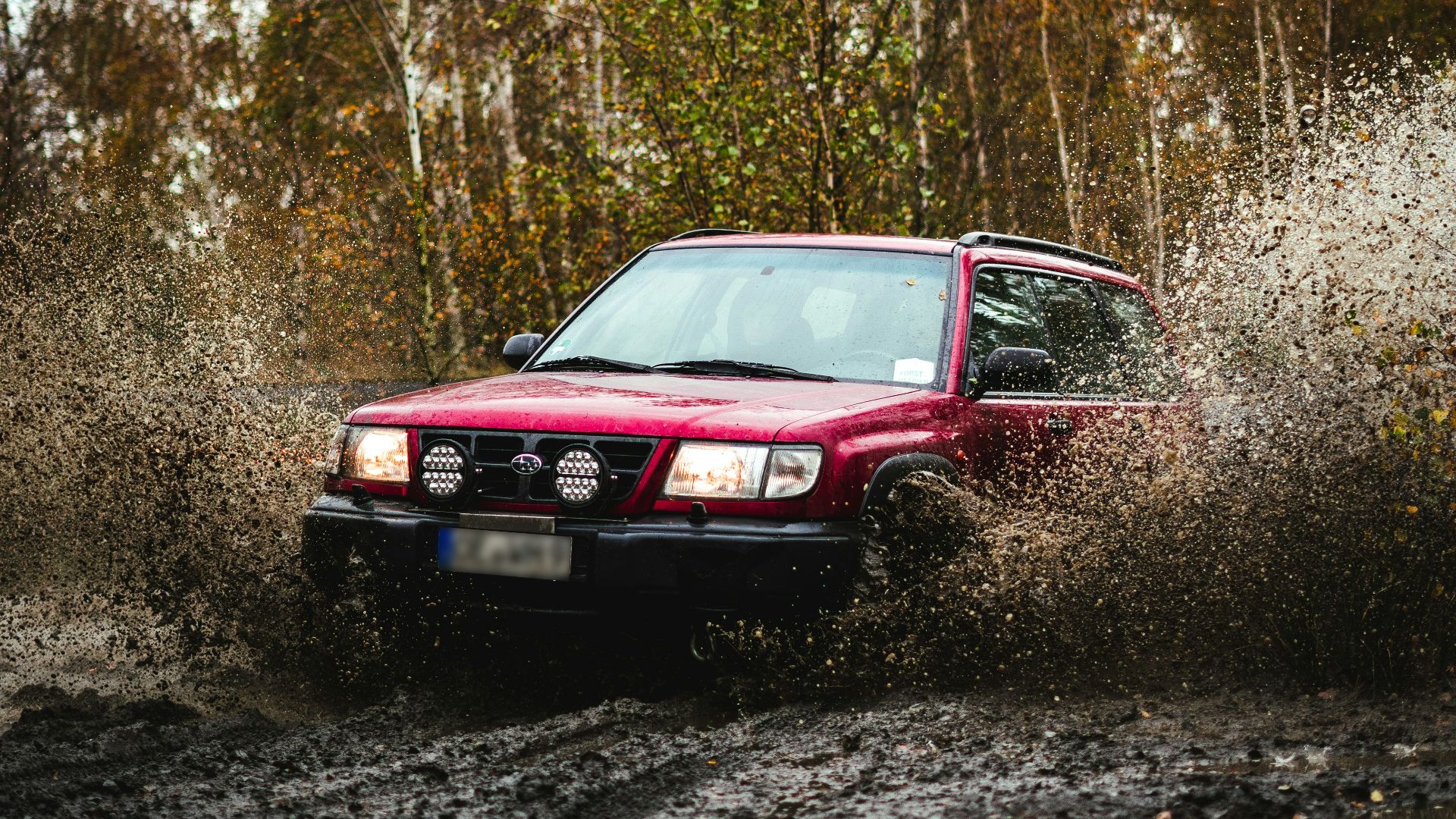 a red car driving through a puddle of mud
