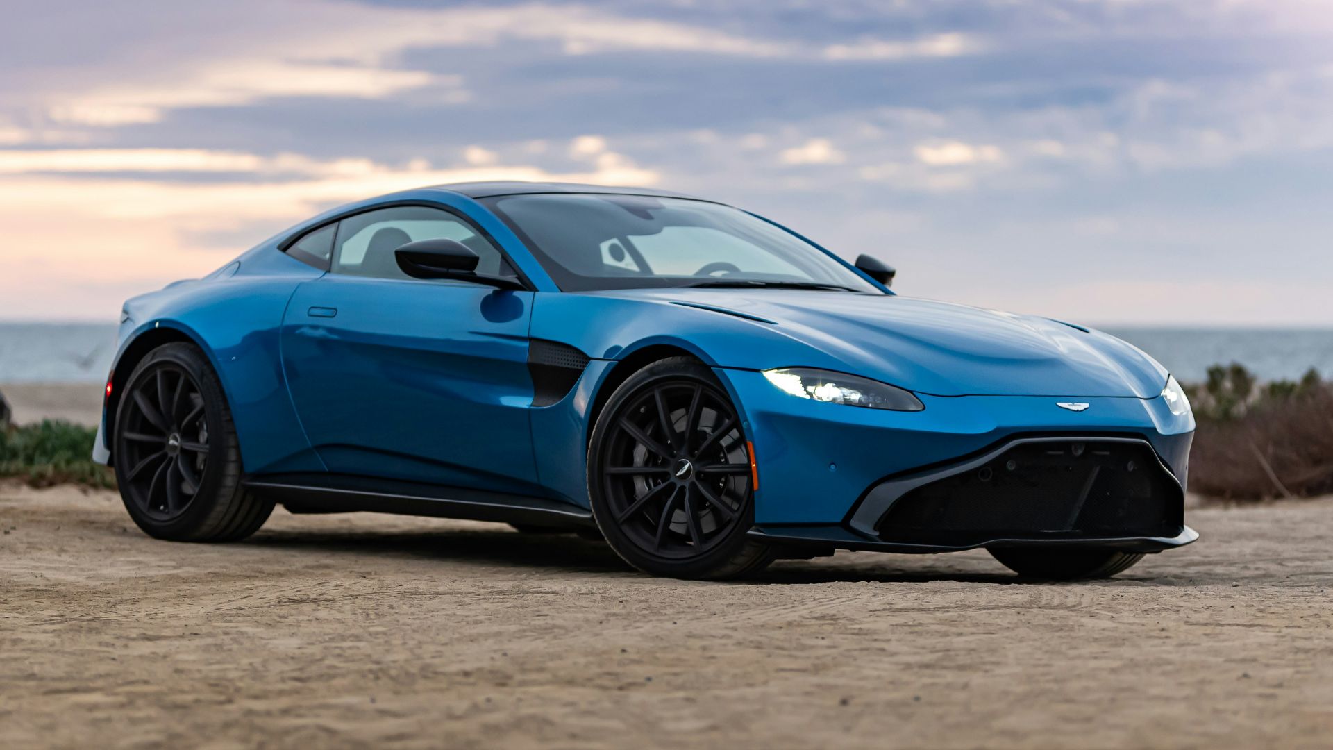 blue porsche 911 on brown sand under white clouds during daytime