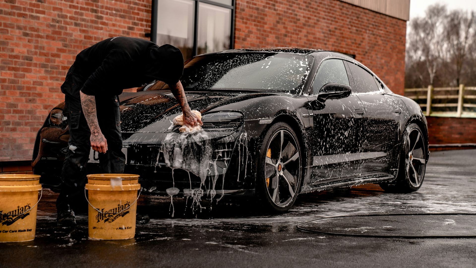 man in black t-shirt and black pants doing water splash on black coupe during daytime