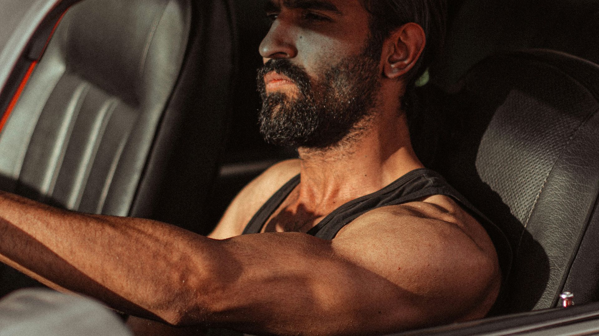 a man sitting in a car with his hand on the steering wheel