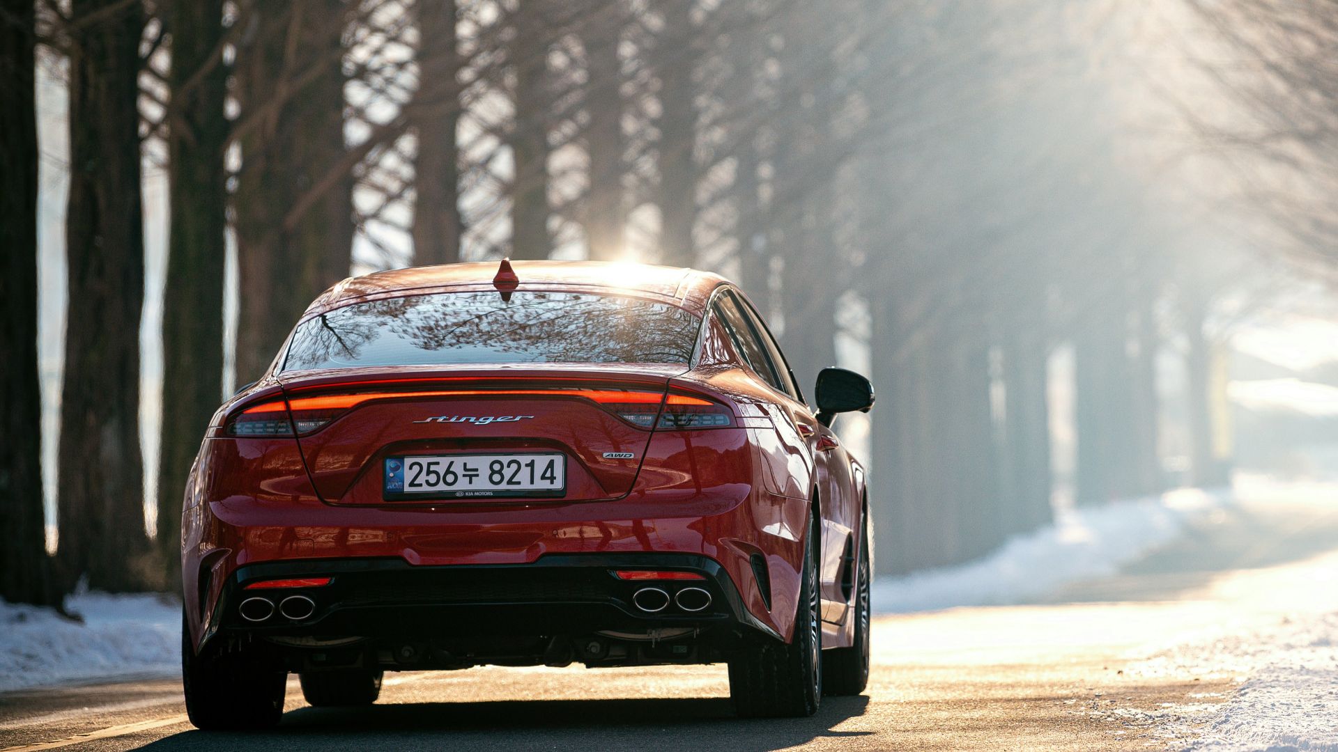 a red car driving on a road with snow on the side