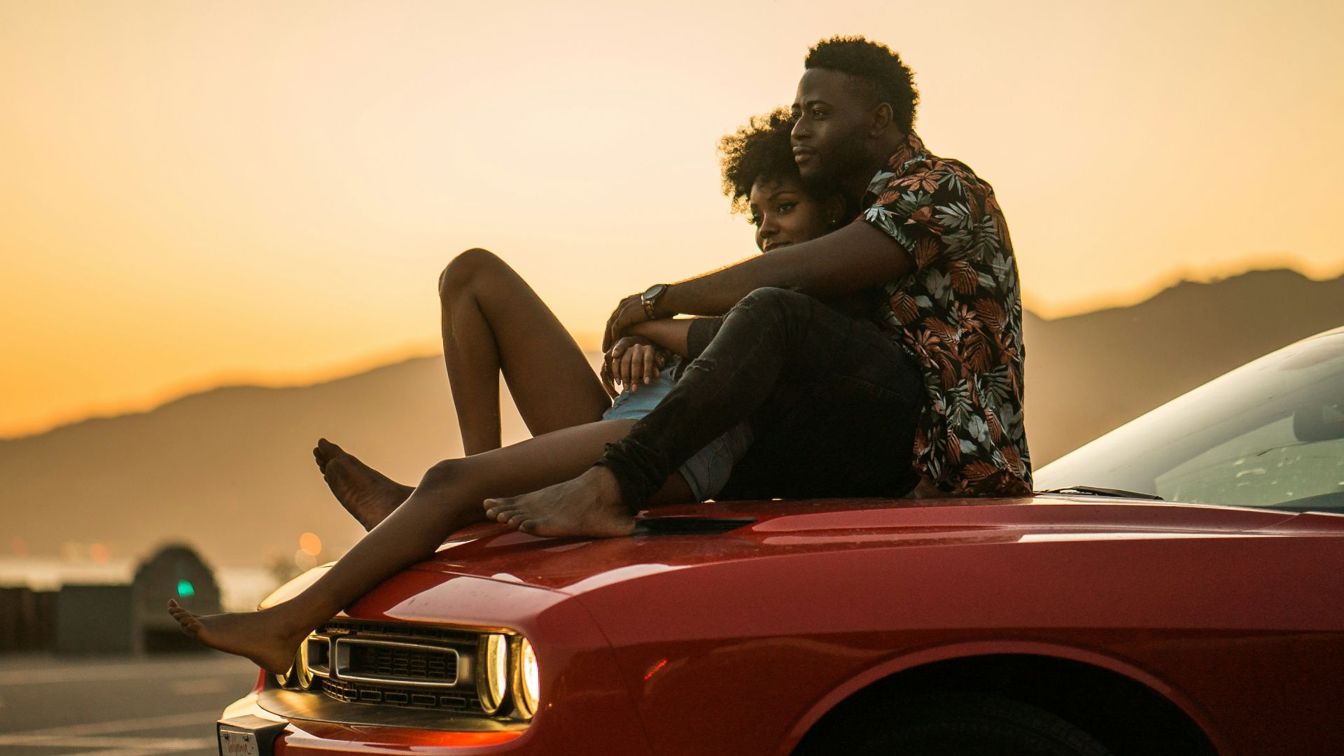 woman in black and white floral dress sitting on red car hood during daytime