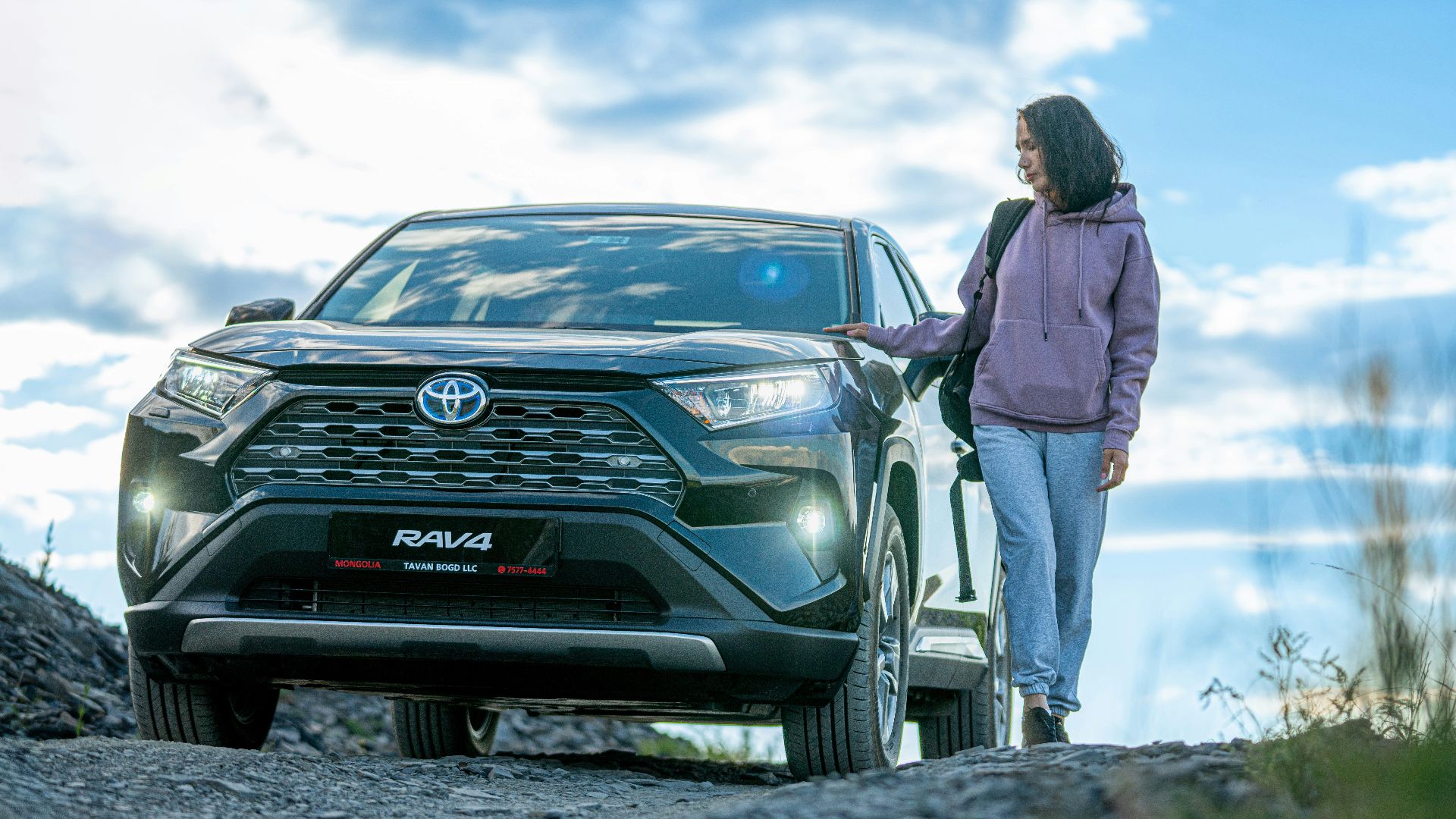 A woman standing next to a car on a dirt road